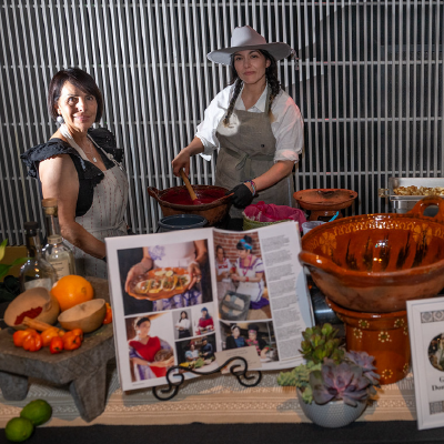 Female chefs preparing traditional Mexican cuisine at a station decorated with authentic cookware and cookbooks.